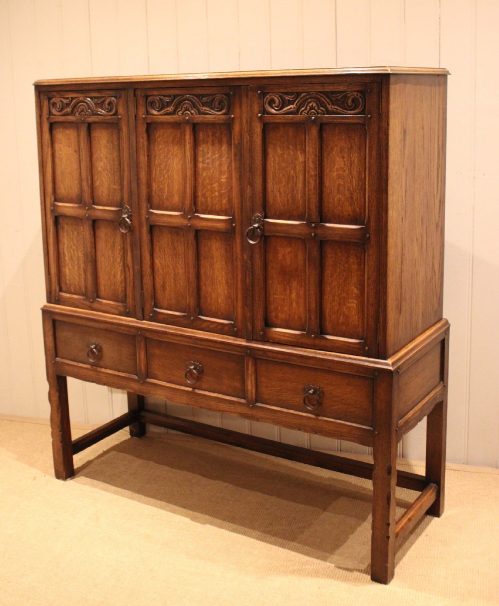 A solid oak side cabinet featuring three carved panel doors above three short drawers on square legs. View IX