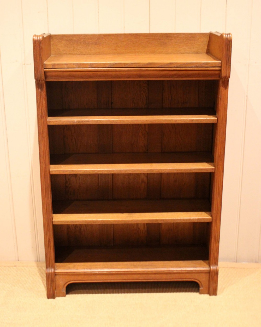 A freestanding light oak open bookcase featuring four horizontal shelves, a raised gallery rail, and curved side brackets. View IV