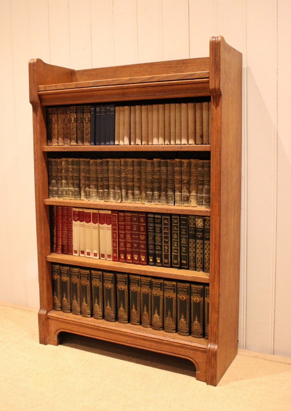 A freestanding light oak open bookcase featuring four horizontal shelves, a raised gallery rail, and curved side brackets. View V