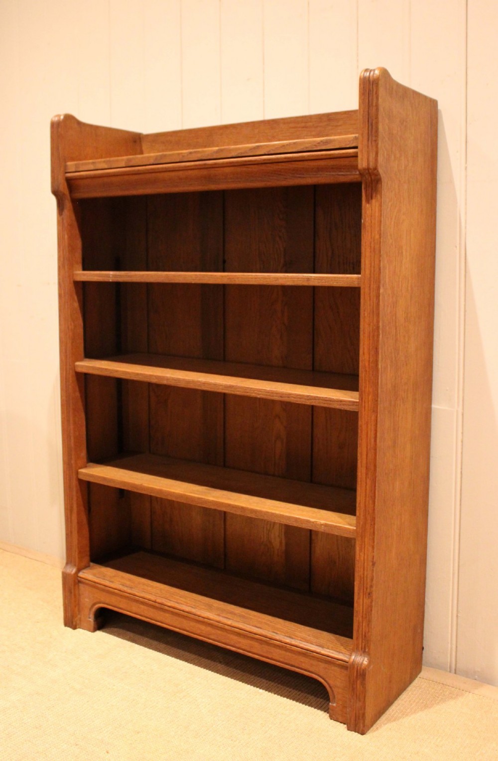 A freestanding light oak open bookcase featuring four horizontal shelves, a raised gallery rail, and curved side brackets. View VI
