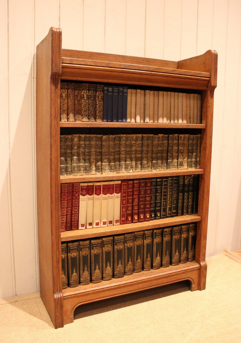 A freestanding light oak open bookcase featuring four horizontal shelves, a raised gallery rail, and curved side brackets. View VII