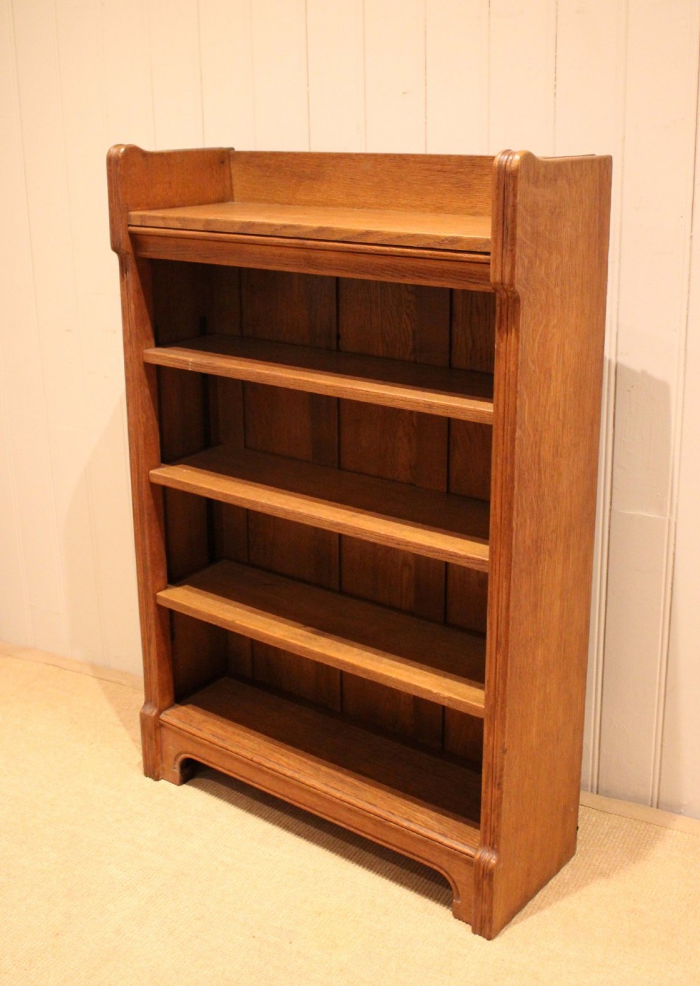 A freestanding light oak open bookcase featuring four horizontal shelves, a raised gallery rail, and curved side brackets. View VIII