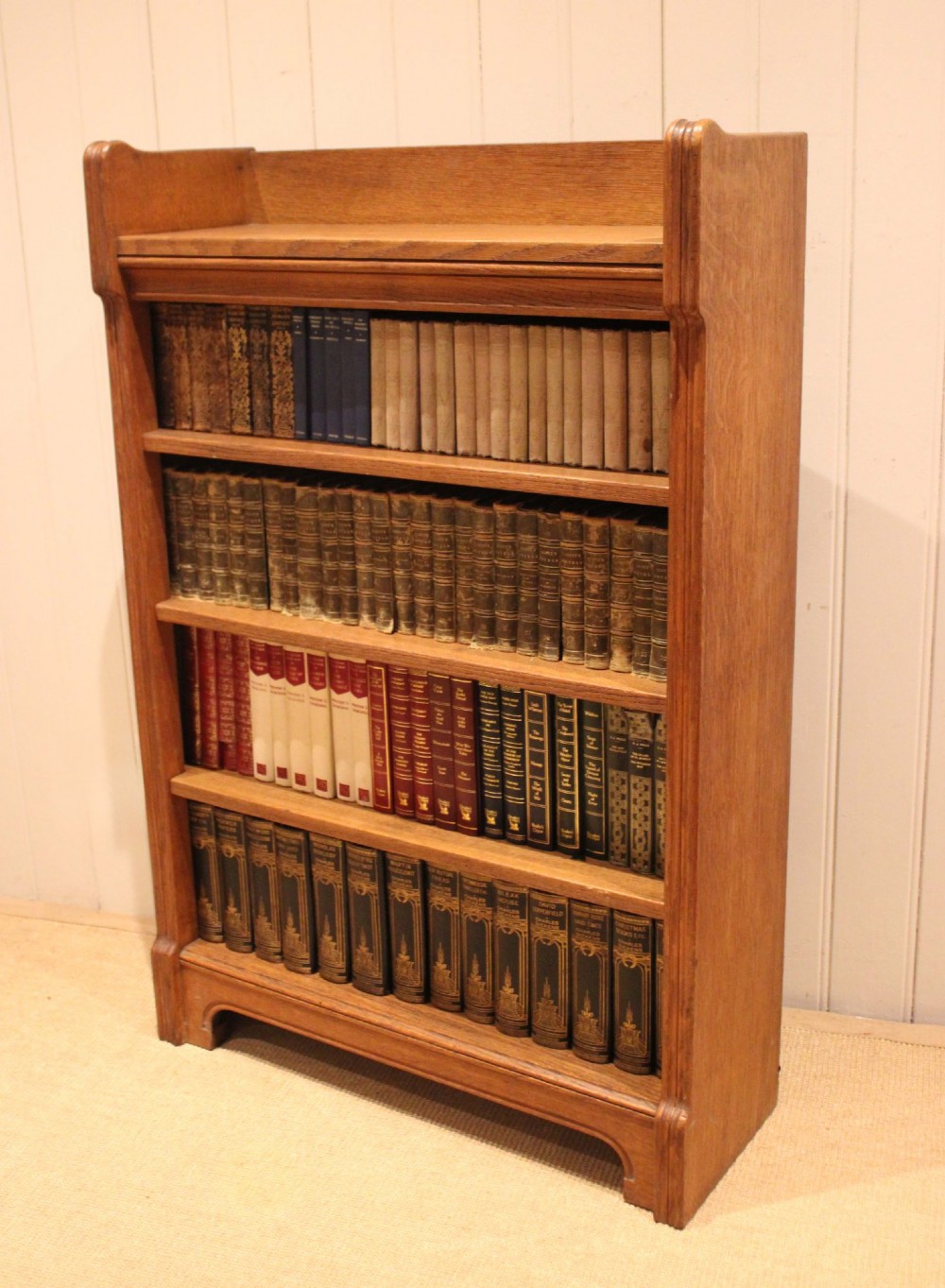A freestanding light oak open bookcase featuring four horizontal shelves, a raised gallery rail, and curved side brackets. View IX
