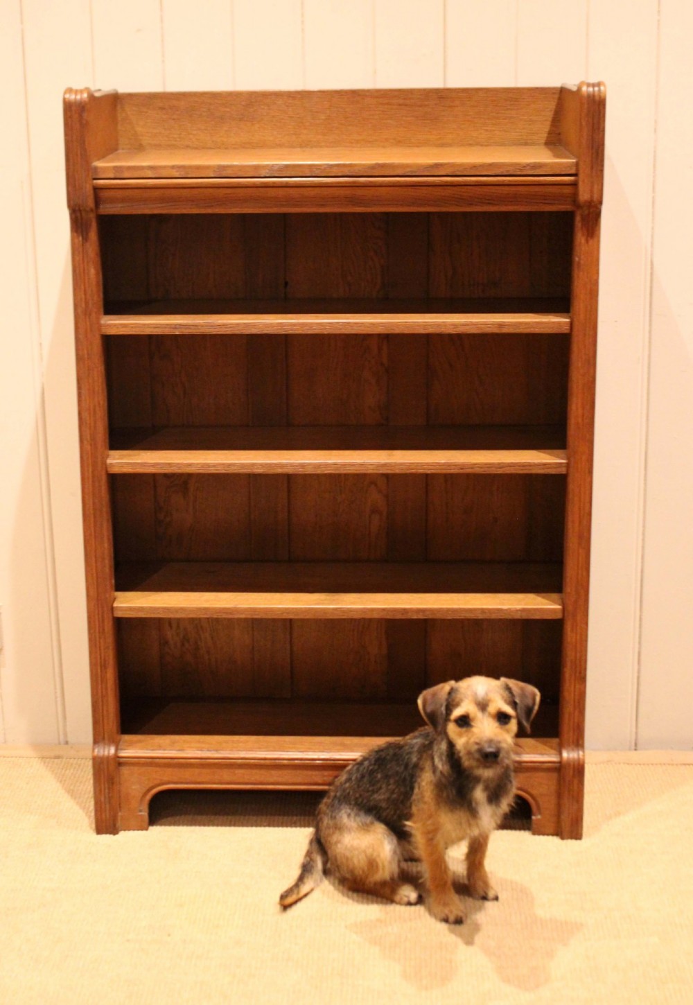 A freestanding light oak open bookcase featuring four horizontal shelves, a raised gallery rail, and curved side brackets. View XII