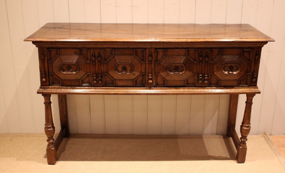 A Jacobean style carved oak dresser base with two geometric moulded drawers, split spindle mouldings, and turned front legs.