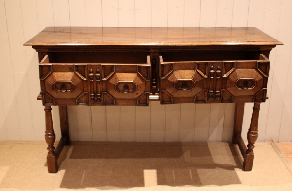 A Jacobean style carved oak dresser base with two geometric moulded drawers, split spindle mouldings, and turned front legs. View II