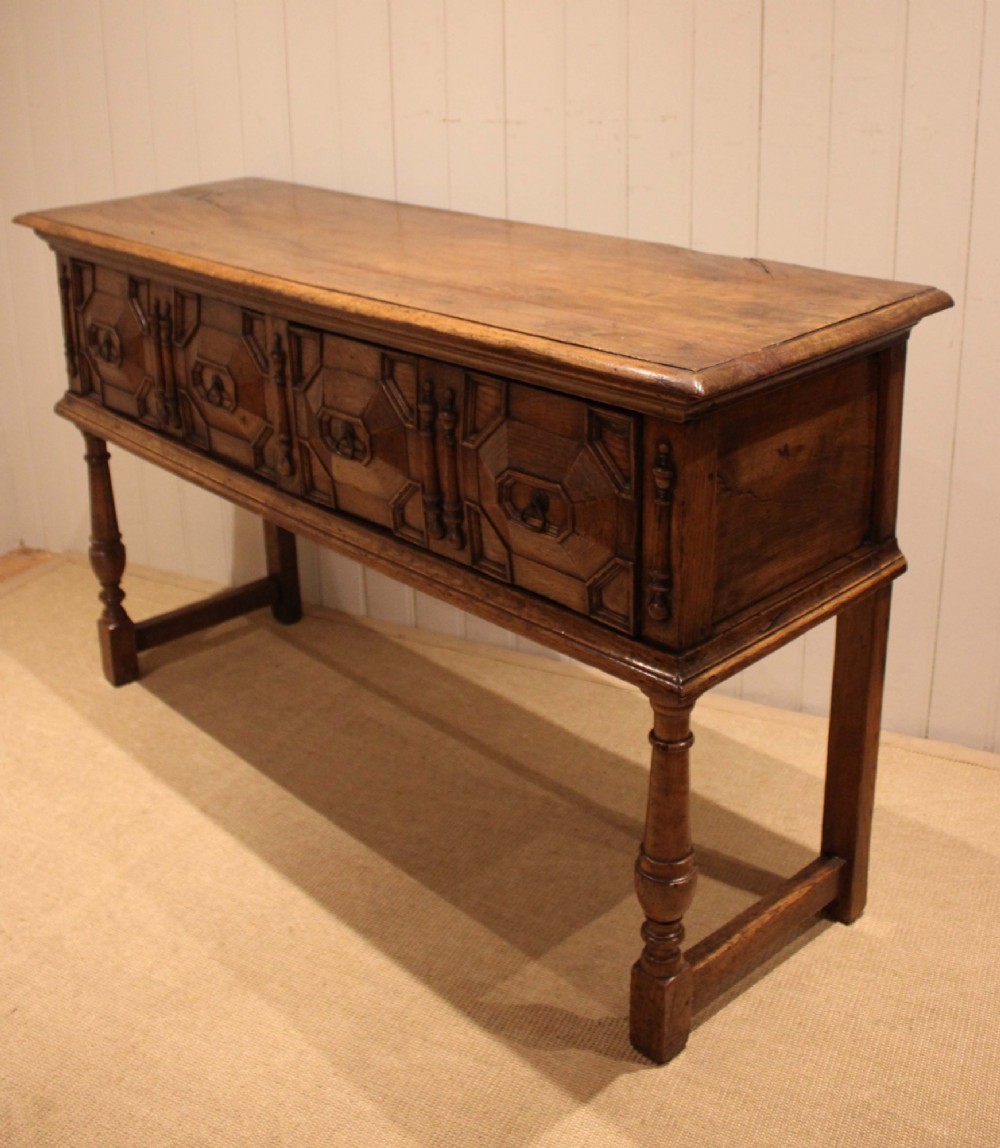 A Jacobean style carved oak dresser base with two geometric moulded drawers, split spindle mouldings, and turned front legs. View III