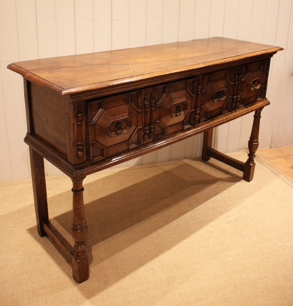 A Jacobean style carved oak dresser base with two geometric moulded drawers, split spindle mouldings, and turned front legs. View IV