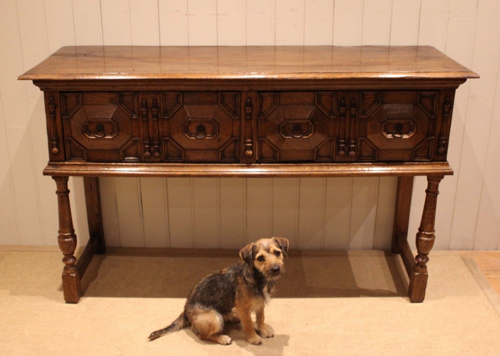 A Jacobean style carved oak dresser base with two geometric moulded drawers, split spindle mouldings, and turned front legs. View VI