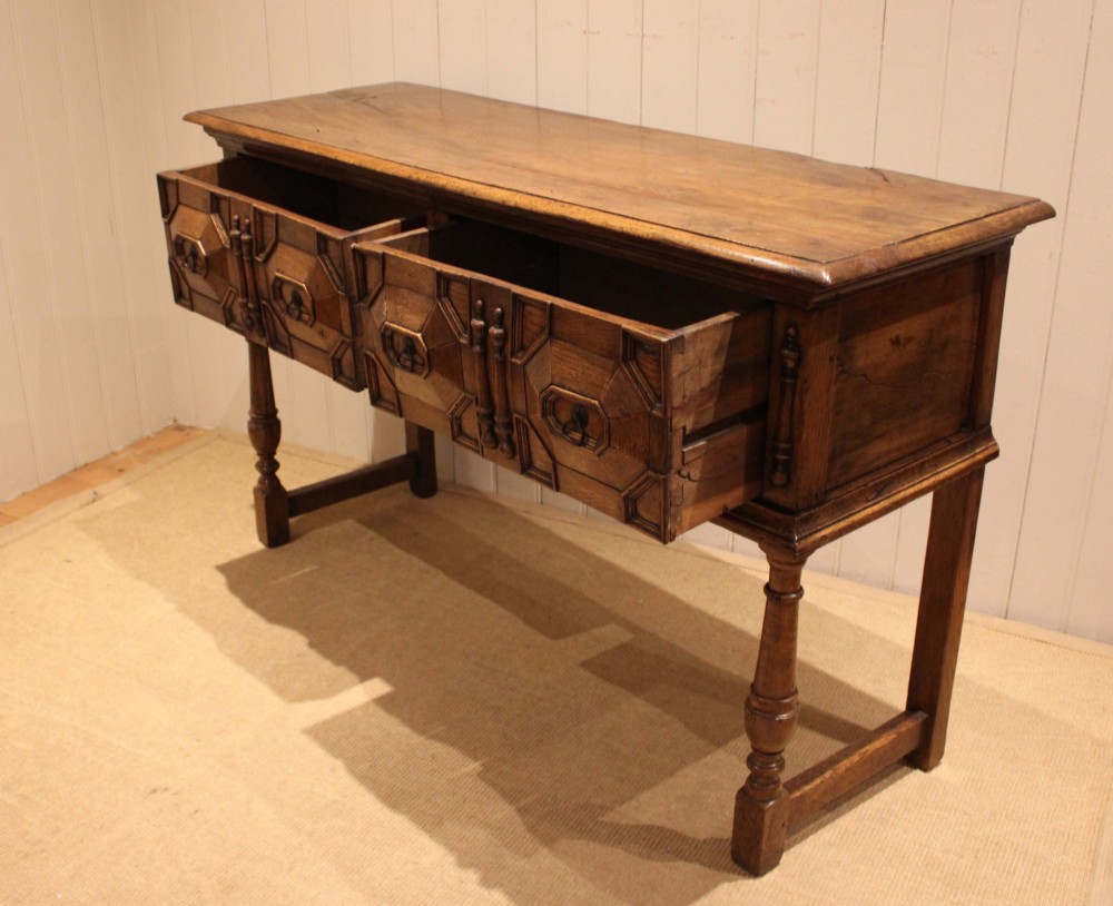 A Jacobean style carved oak dresser base with two geometric moulded drawers, split spindle mouldings, and turned front legs. View VII