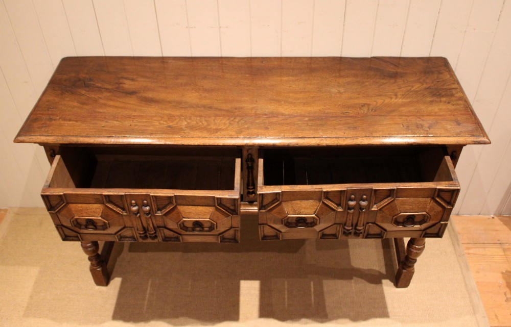 A Jacobean style carved oak dresser base with two geometric moulded drawers, split spindle mouldings, and turned front legs. View IX