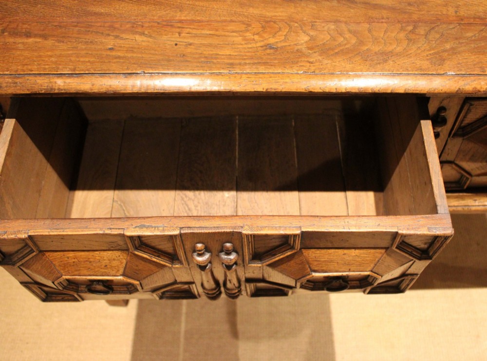 A Jacobean style carved oak dresser base with two geometric moulded drawers, split spindle mouldings, and turned front legs. View XI