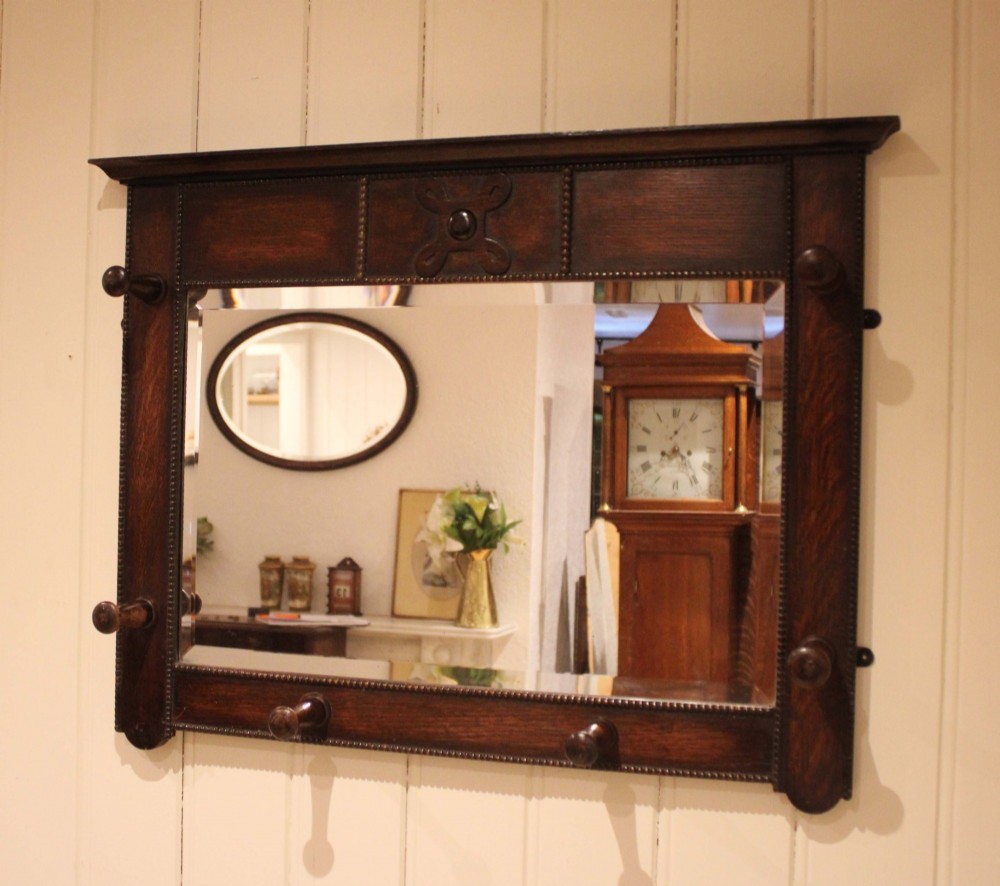 A dark oak rectangular wall mirror featuring six turned wooden coat pegs framing the glass plate, decorated with beaded trim and a carved central boss on the top rail.