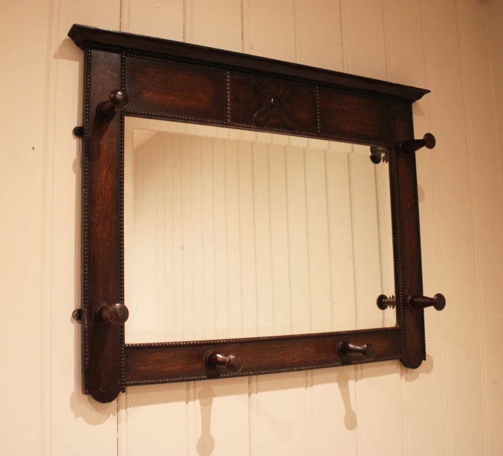 A dark oak rectangular wall mirror featuring six turned wooden coat pegs framing the glass plate, decorated with beaded trim and a carved central boss on the top rail. View II