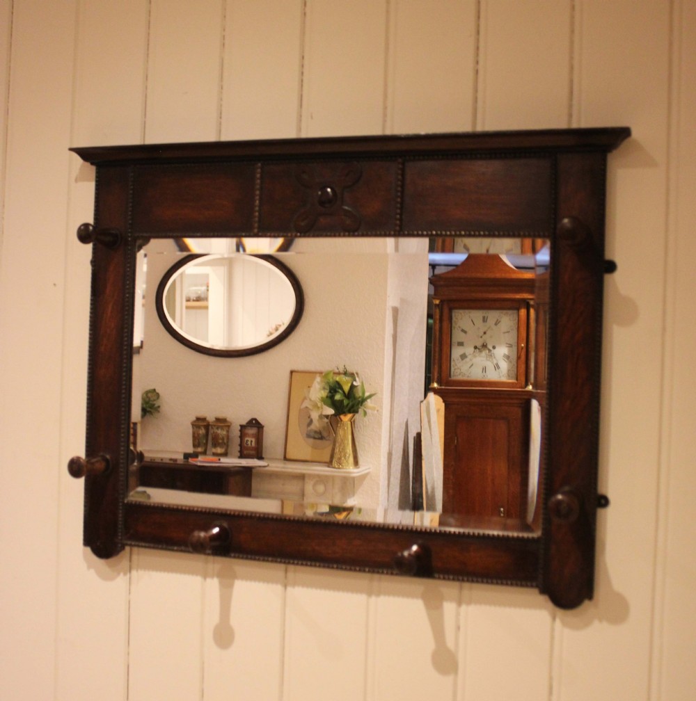 A dark oak rectangular wall mirror featuring six turned wooden coat pegs framing the glass plate, decorated with beaded trim and a carved central boss on the top rail. View III