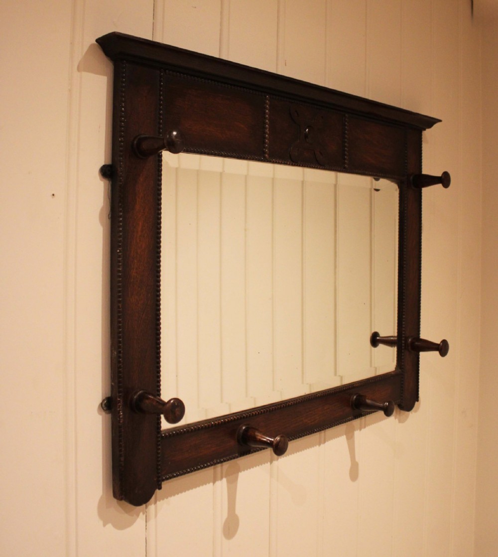 A dark oak rectangular wall mirror featuring six turned wooden coat pegs framing the glass plate, decorated with beaded trim and a carved central boss on the top rail. View IV