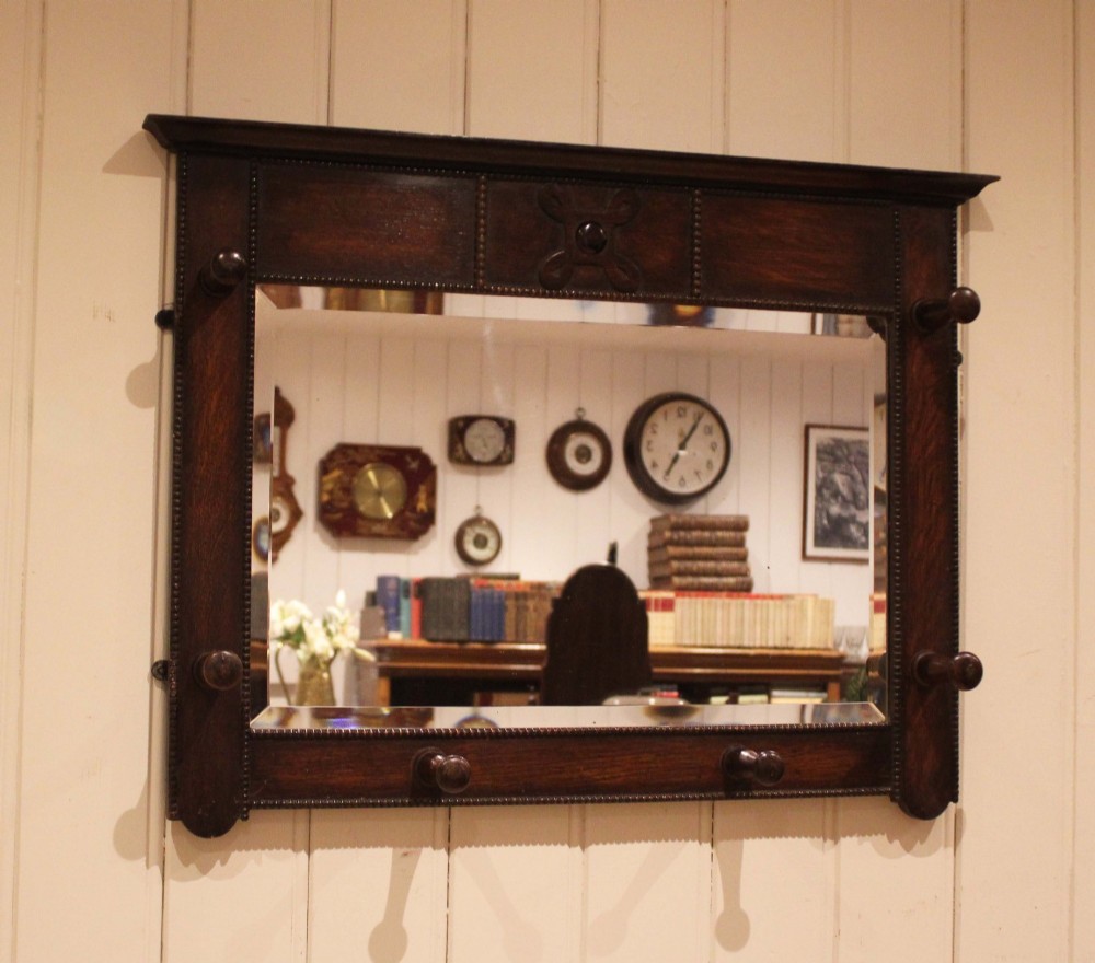 A dark oak rectangular wall mirror featuring six turned wooden coat pegs framing the glass plate, decorated with beaded trim and a carved central boss on the top rail. View V