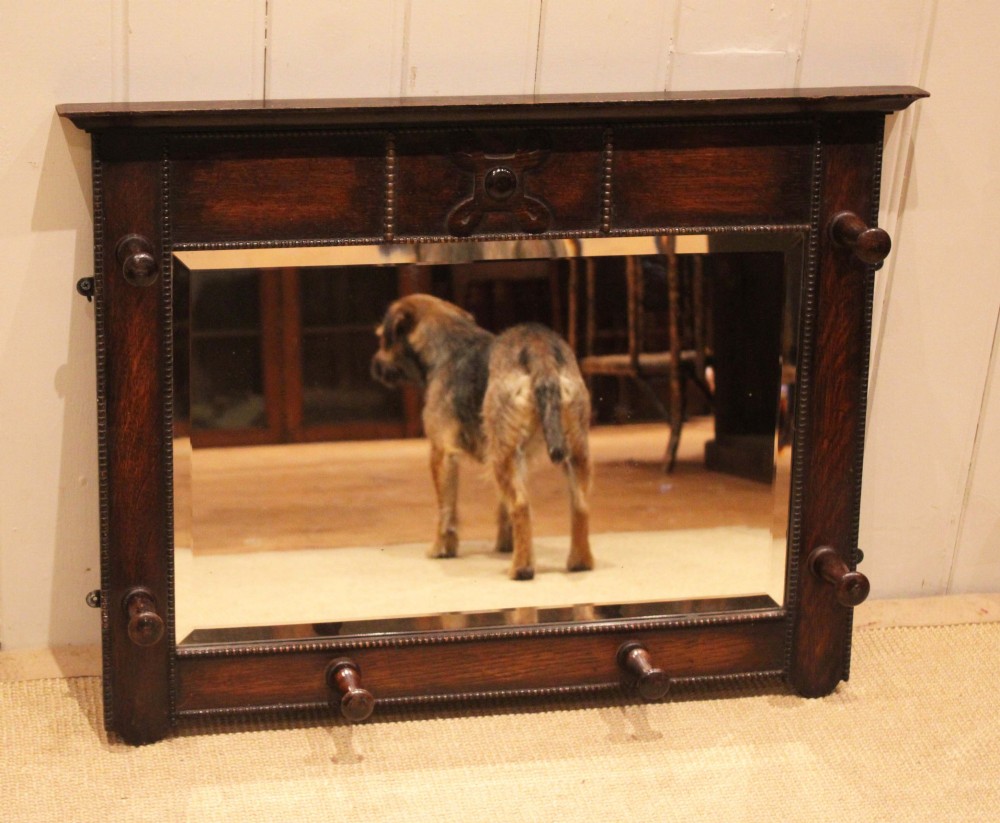 A dark oak rectangular wall mirror featuring six turned wooden coat pegs framing the glass plate, decorated with beaded trim and a carved central boss on the top rail. View VII