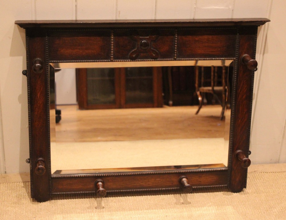 A dark oak rectangular wall mirror featuring six turned wooden coat pegs framing the glass plate, decorated with beaded trim and a carved central boss on the top rail. View VIII
