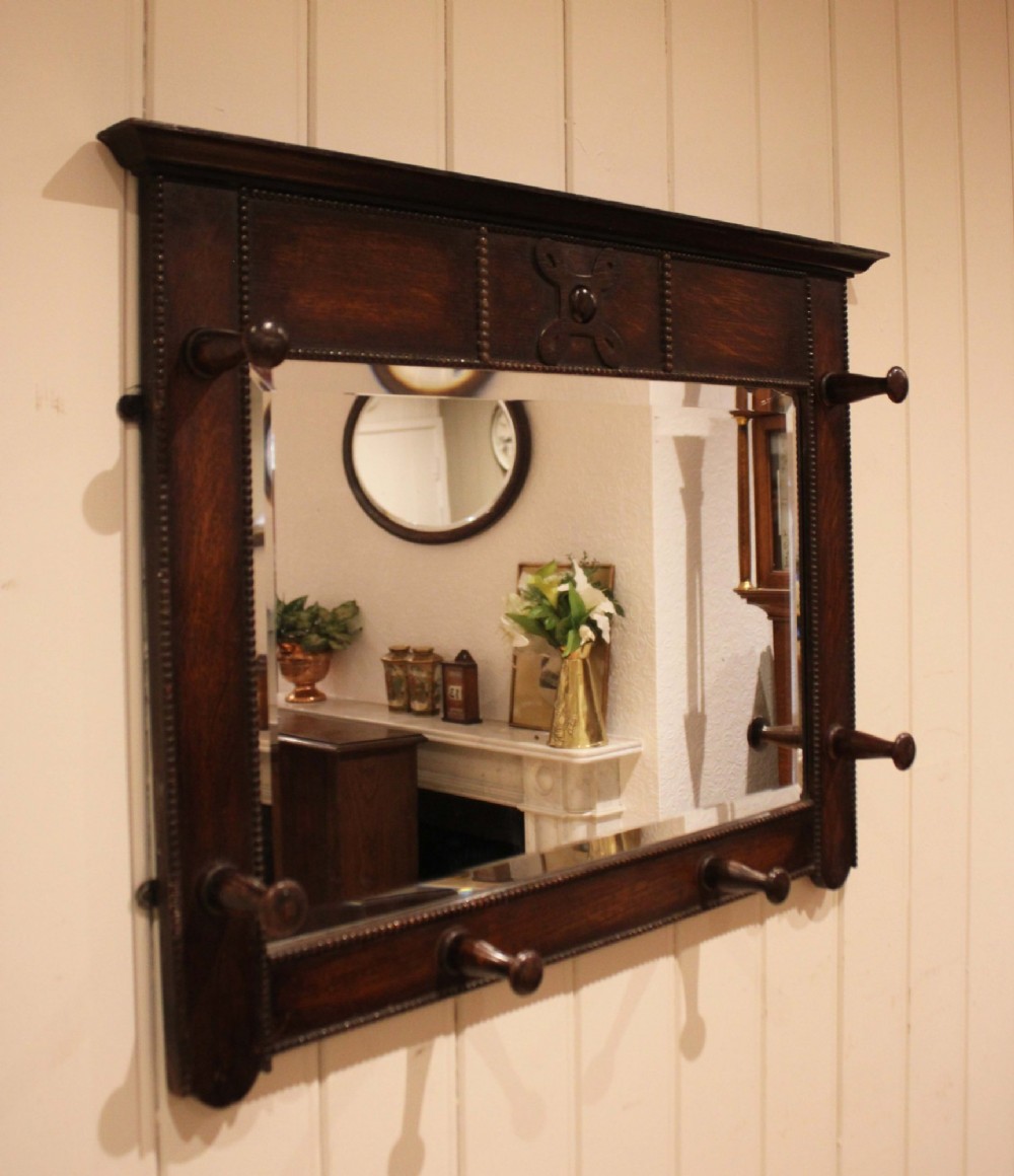 A dark oak rectangular wall mirror featuring six turned wooden coat pegs framing the glass plate, decorated with beaded trim and a carved central boss on the top rail. View IX