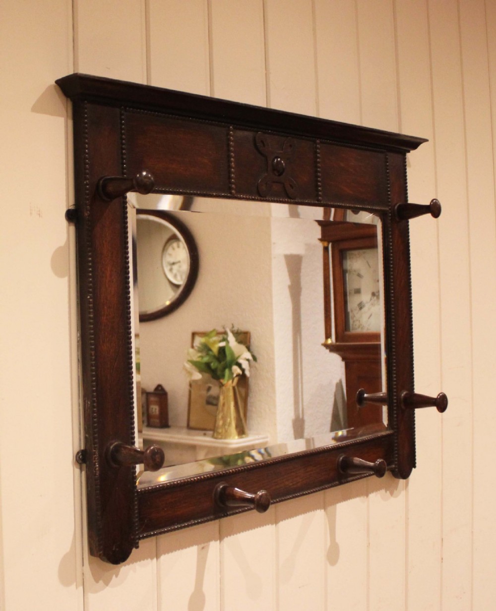 A dark oak rectangular wall mirror featuring six turned wooden coat pegs framing the glass plate, decorated with beaded trim and a carved central boss on the top rail. View XI