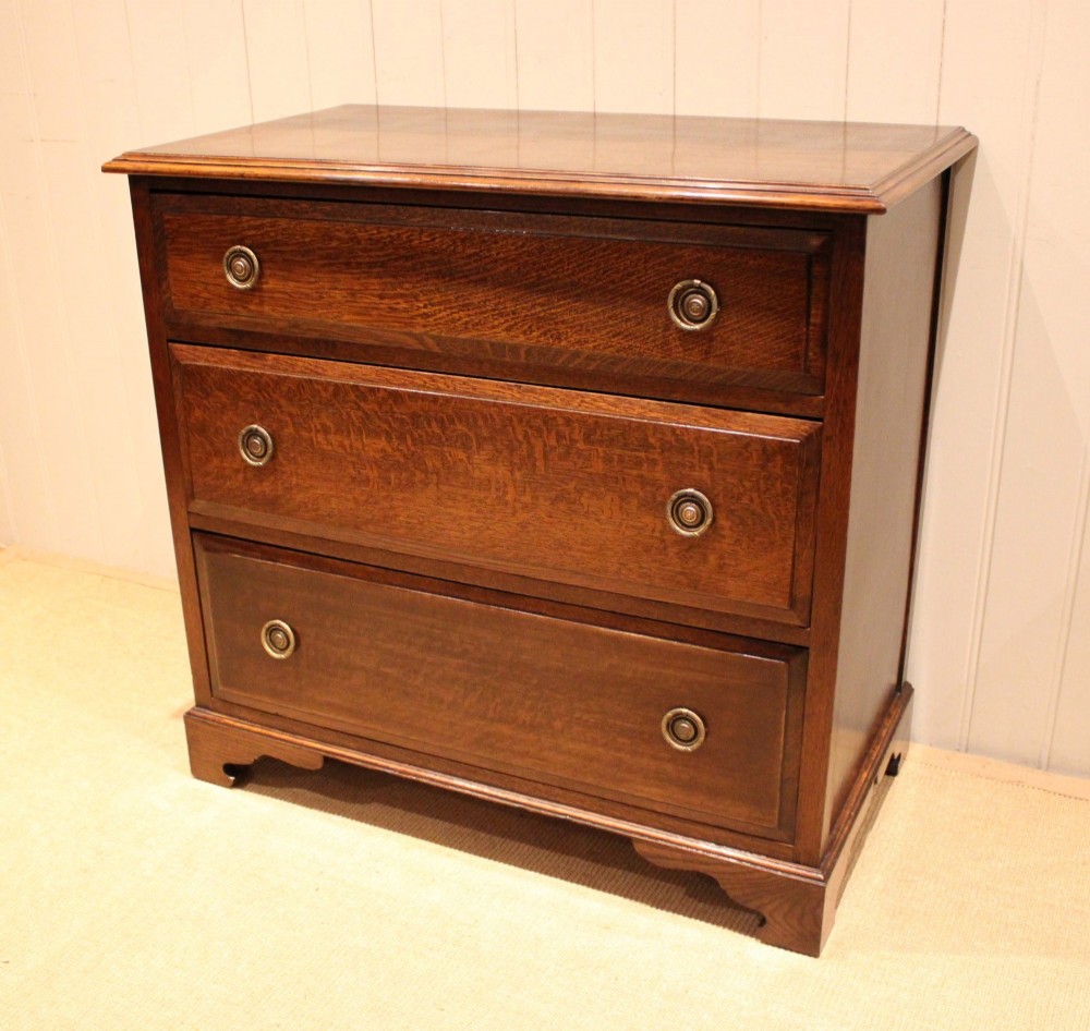 A solid oak chest of drawers featuring three full-width drawers with circular brass drop ring handles and bracket feet.