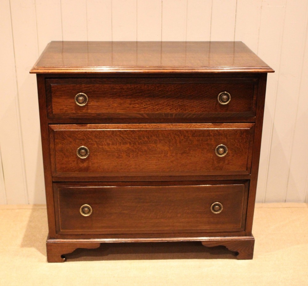 A solid oak chest of drawers featuring three full-width drawers with circular brass drop ring handles and bracket feet. View II