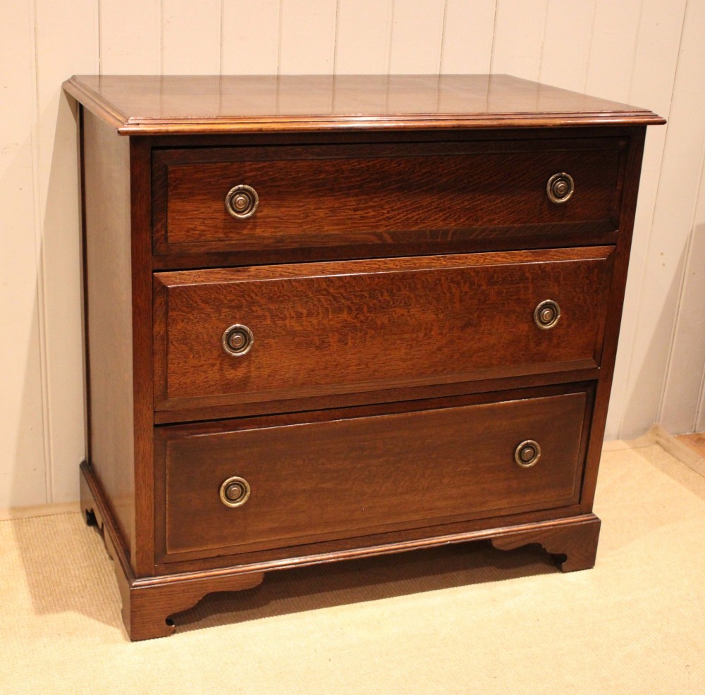 A solid oak chest of drawers featuring three full-width drawers with circular brass drop ring handles and bracket feet. View III