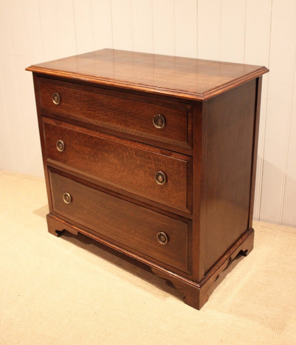 A solid oak chest of drawers featuring three full-width drawers with circular brass drop ring handles and bracket feet. View IV