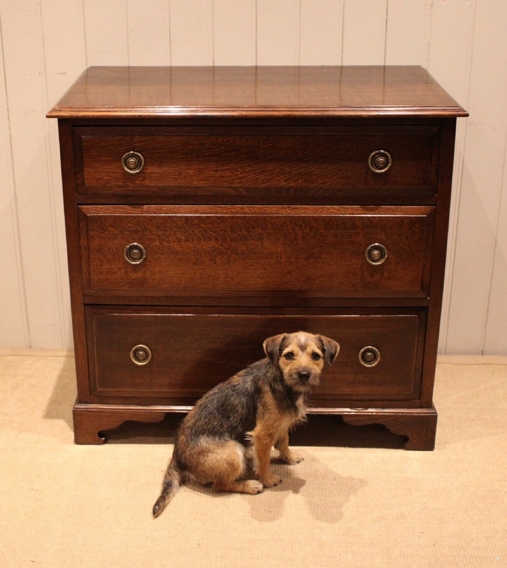 A solid oak chest of drawers featuring three full-width drawers with circular brass drop ring handles and bracket feet. View VII