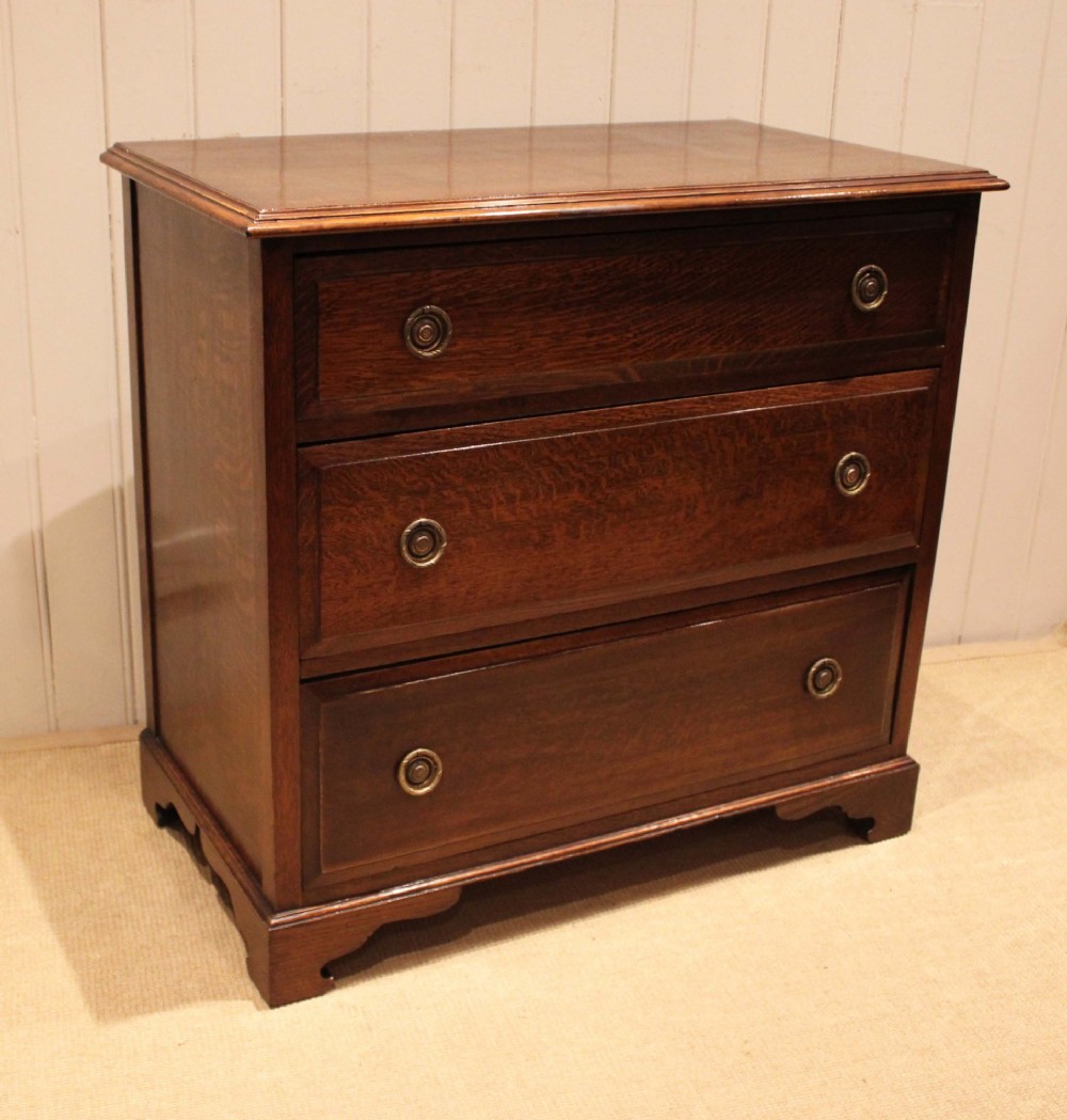 A solid oak chest of drawers featuring three full-width drawers with circular brass drop ring handles and bracket feet. View X