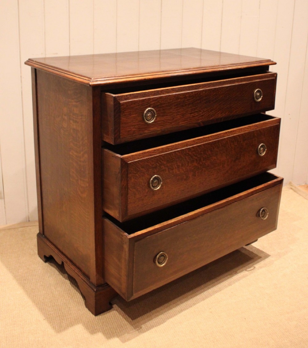 A solid oak chest of drawers featuring three full-width drawers with circular brass drop ring handles and bracket feet. View XI