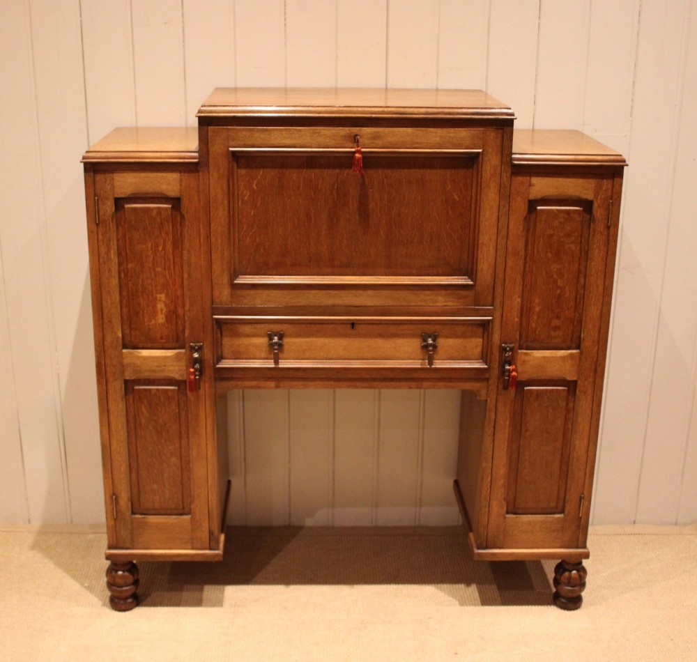 An antique oak bureau cabinet featuring a central fall-front writing compartment above a single drawer, flanked by two side cupboards with panelled doors and raised on turned feet.