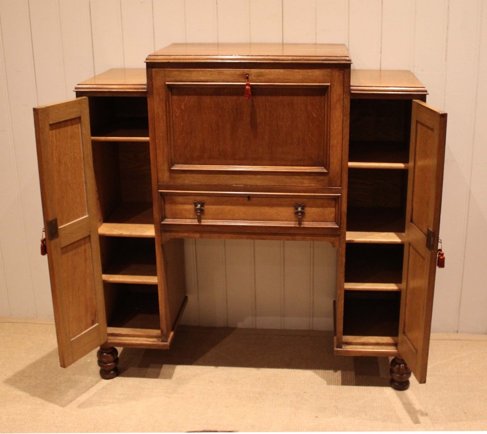 An antique oak bureau cabinet featuring a central fall-front writing compartment above a single drawer, flanked by two side cupboards with panelled doors and raised on turned feet. View IV