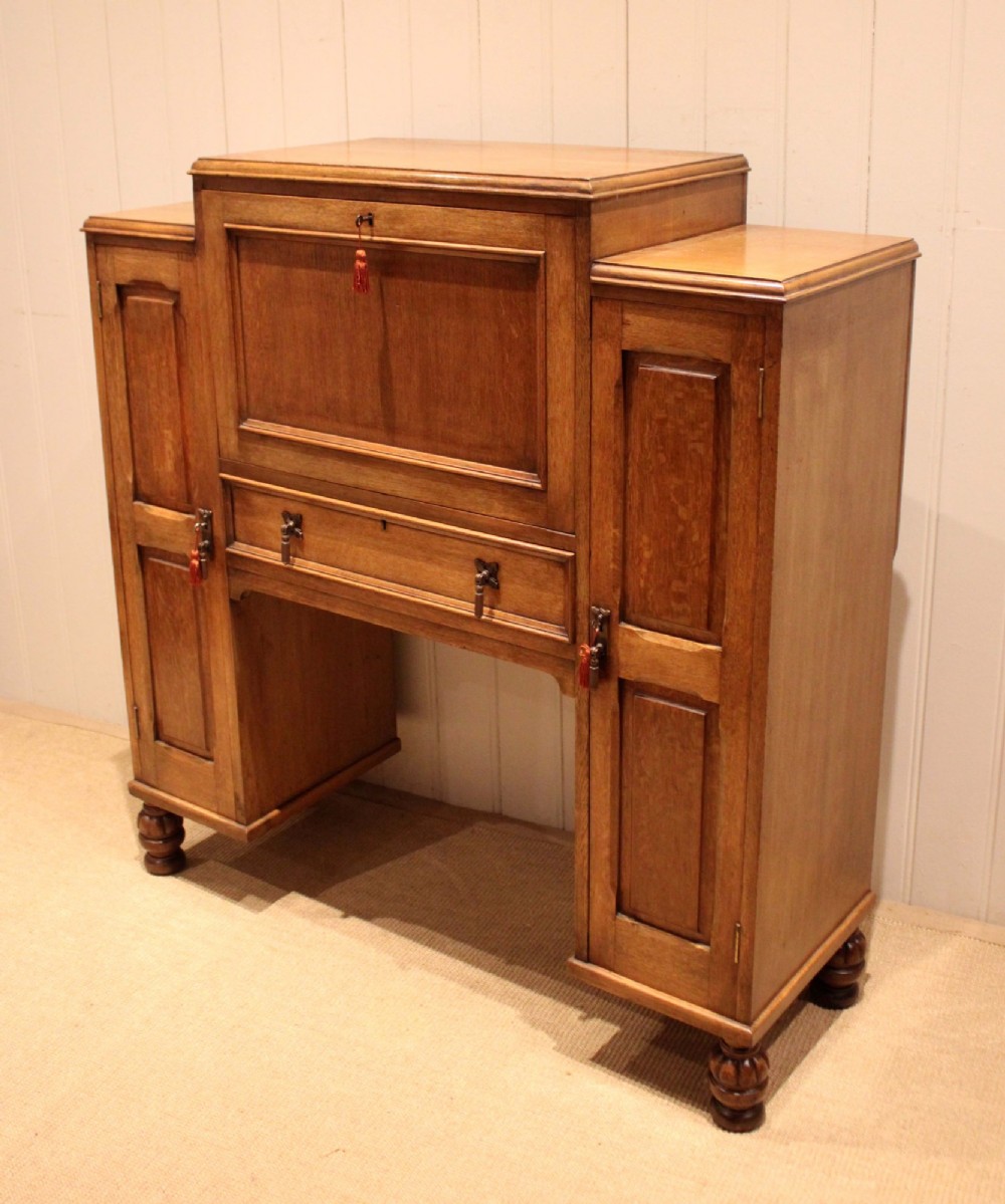 An antique oak bureau cabinet featuring a central fall-front writing compartment above a single drawer, flanked by two side cupboards with panelled doors and raised on turned feet. View IX
