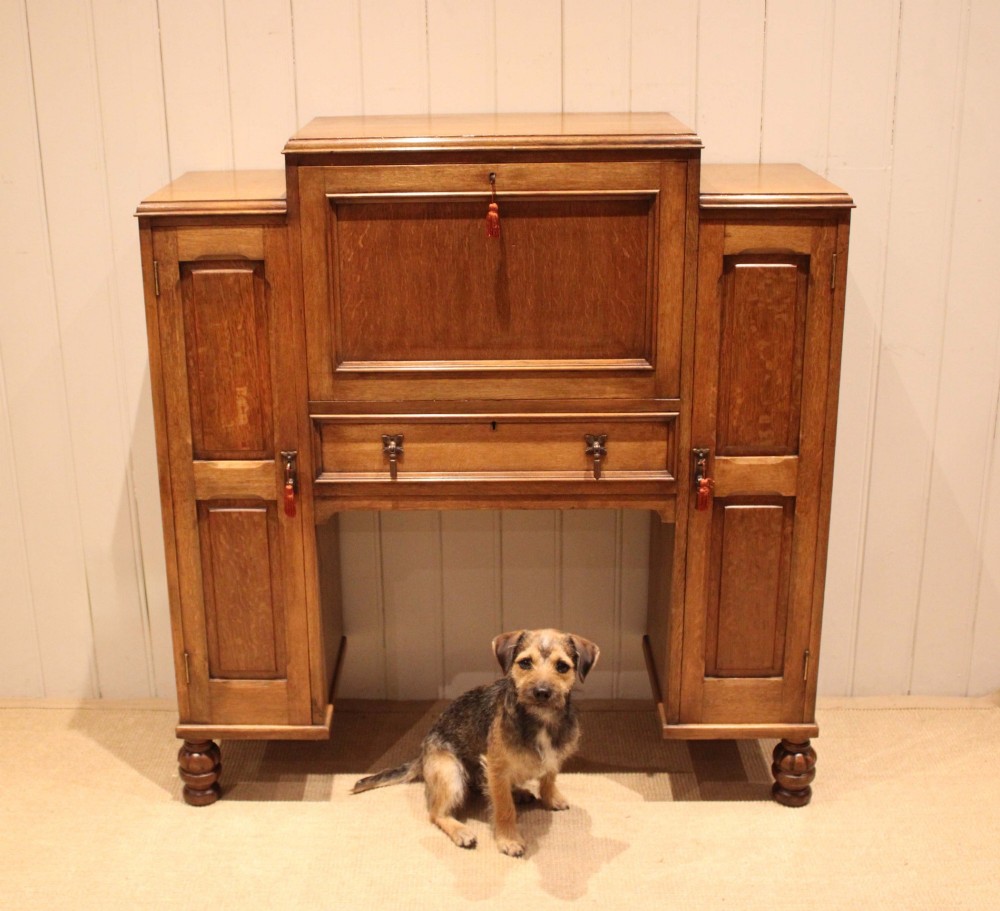 An antique oak bureau cabinet featuring a central fall-front writing compartment above a single drawer, flanked by two side cupboards with panelled doors and raised on turned feet. View XI
