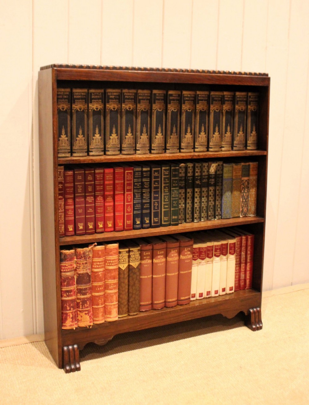 A low dark oak open bookcase with three shelving tiers, a beaded top edge, and fluted bracket feet. View II