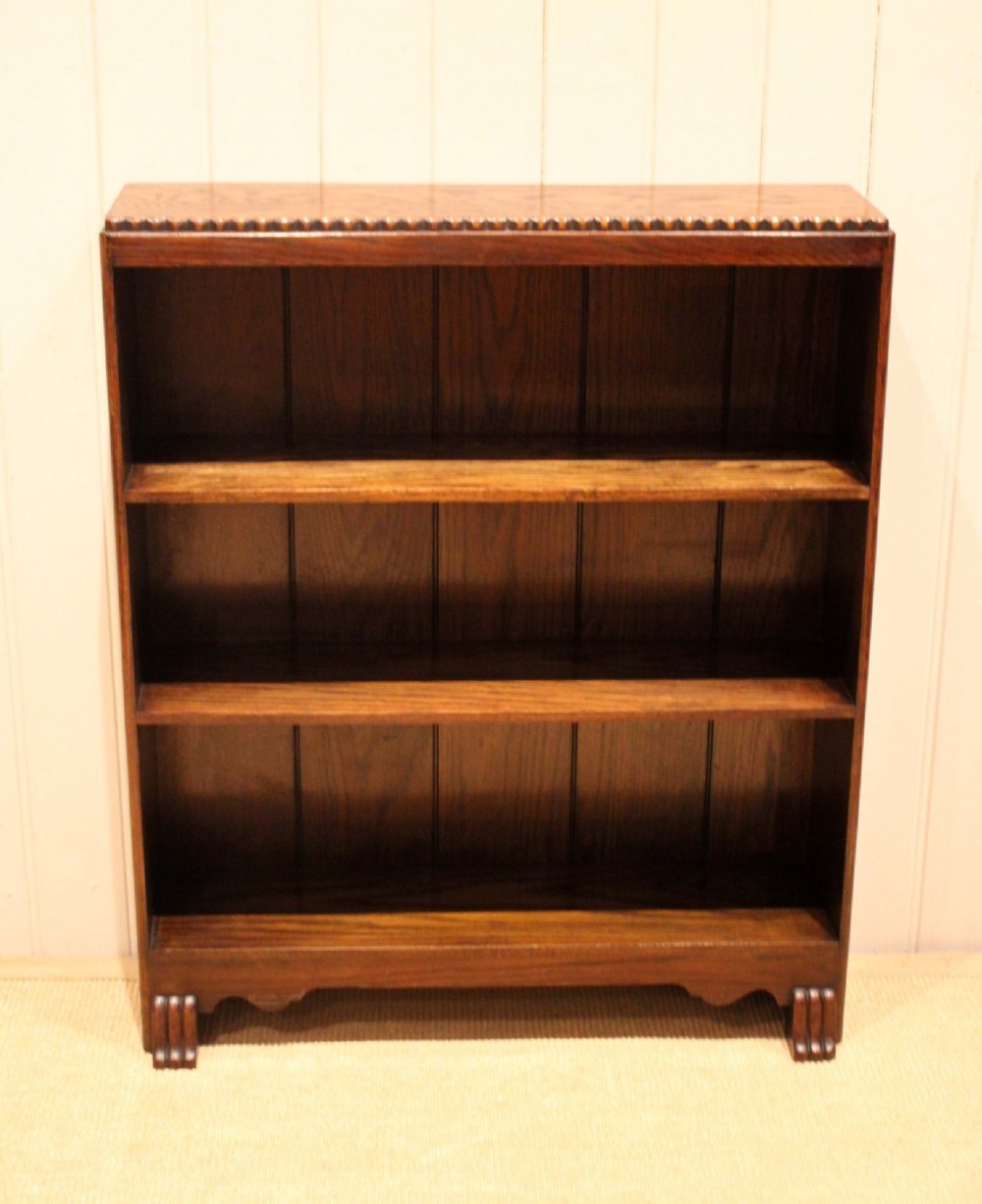 A low dark oak open bookcase with three shelving tiers, a beaded top edge, and fluted bracket feet.