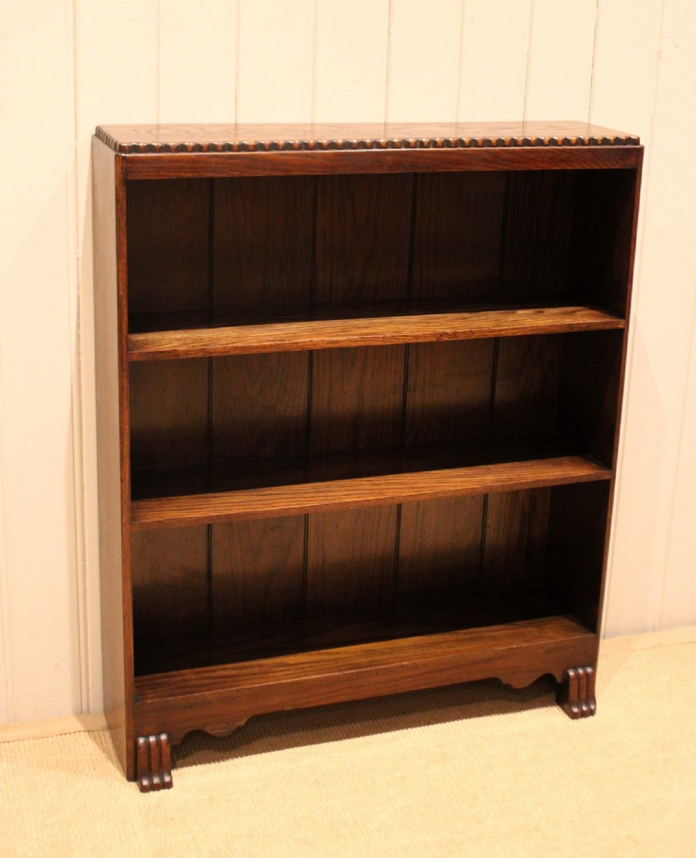 A low dark oak open bookcase with three shelving tiers, a beaded top edge, and fluted bracket feet. View IV