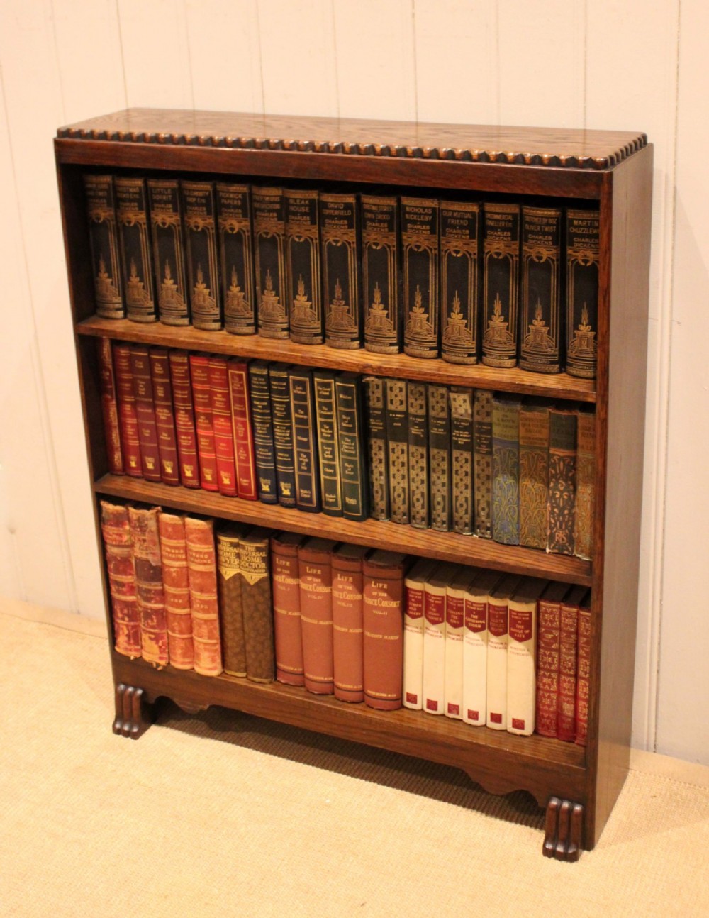 A low dark oak open bookcase with three shelving tiers, a beaded top edge, and fluted bracket feet. View V