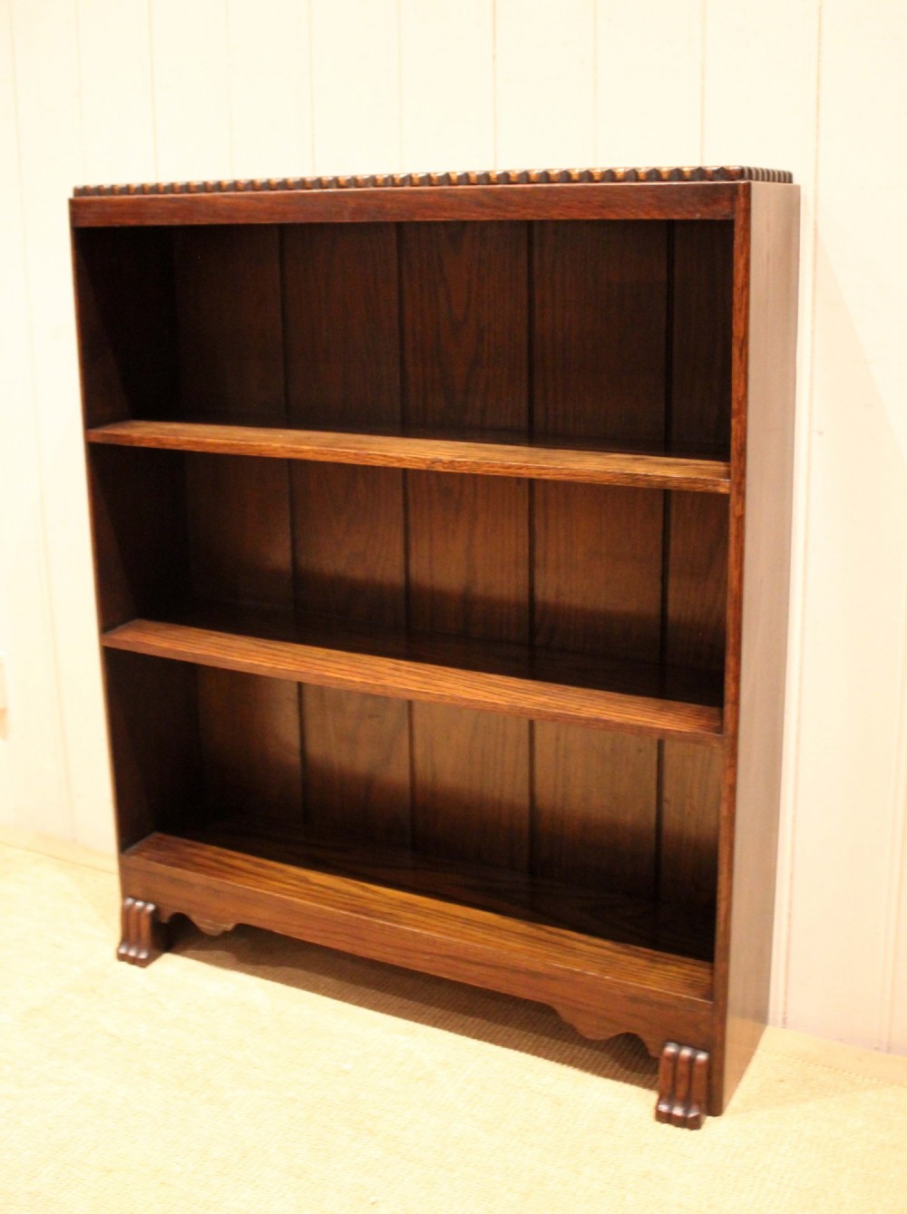 A low dark oak open bookcase with three shelving tiers, a beaded top edge, and fluted bracket feet. View VI