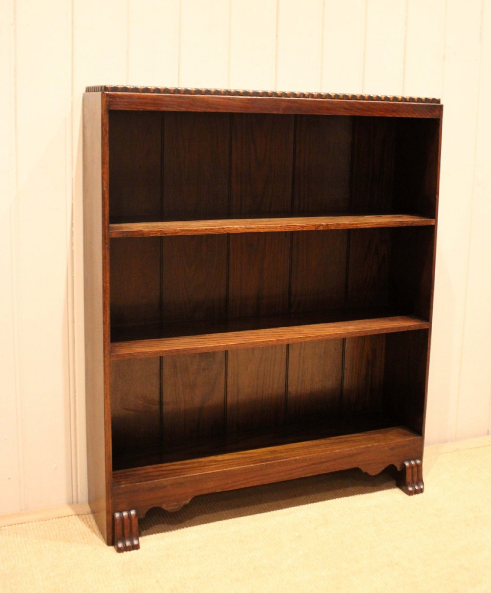 A low dark oak open bookcase with three shelving tiers, a beaded top edge, and fluted bracket feet. View VIII