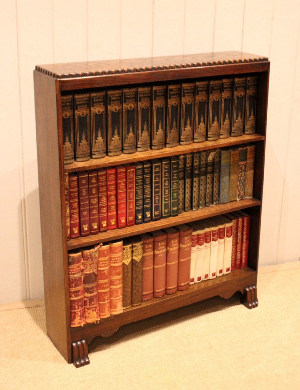A low dark oak open bookcase with three shelving tiers, a beaded top edge, and fluted bracket feet. View IX