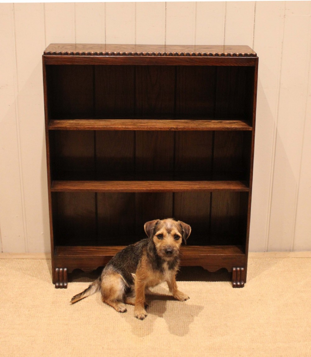A low dark oak open bookcase with three shelving tiers, a beaded top edge, and fluted bracket feet. View X