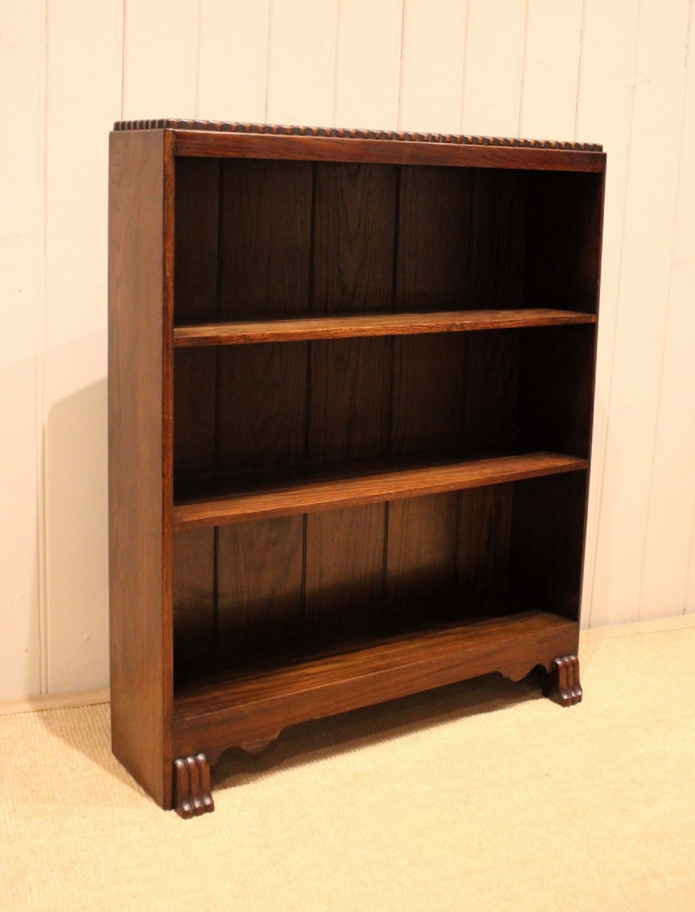 A low dark oak open bookcase with three shelving tiers, a beaded top edge, and fluted bracket feet. View XII