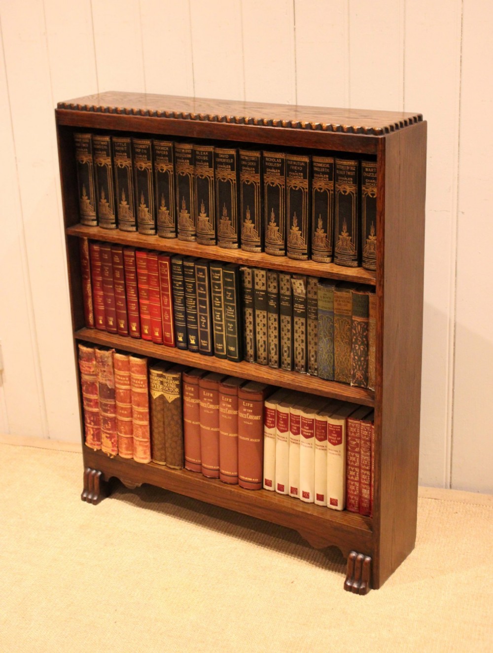 A low dark oak open bookcase with three shelving tiers, a beaded top edge, and fluted bracket feet. View XIII
