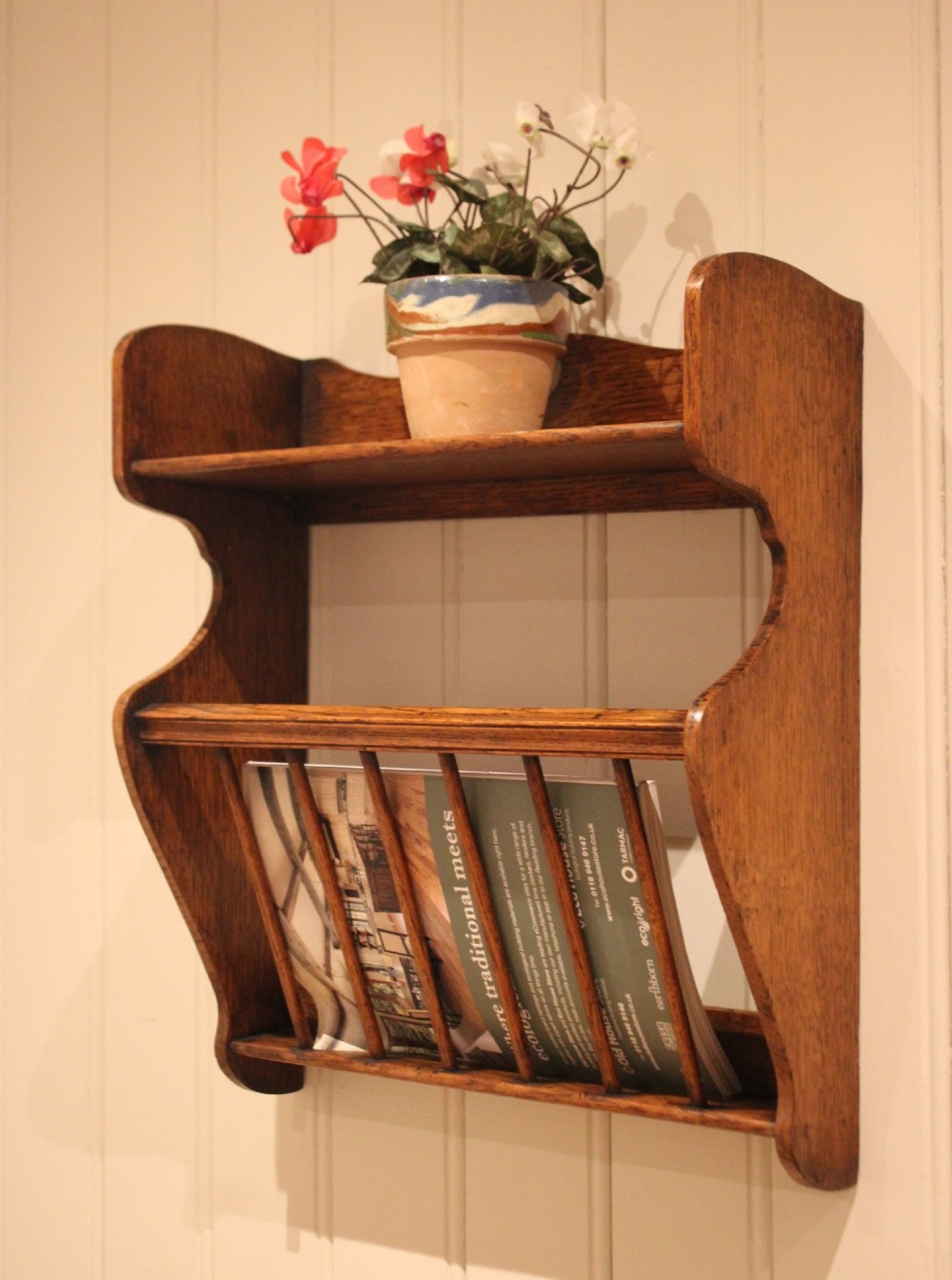 An Arts and Crafts solid oak wall shelf featuring a top shelf ledge with a pierced heart cutout and a lower magazine rack with vertical wooden spindles. View II