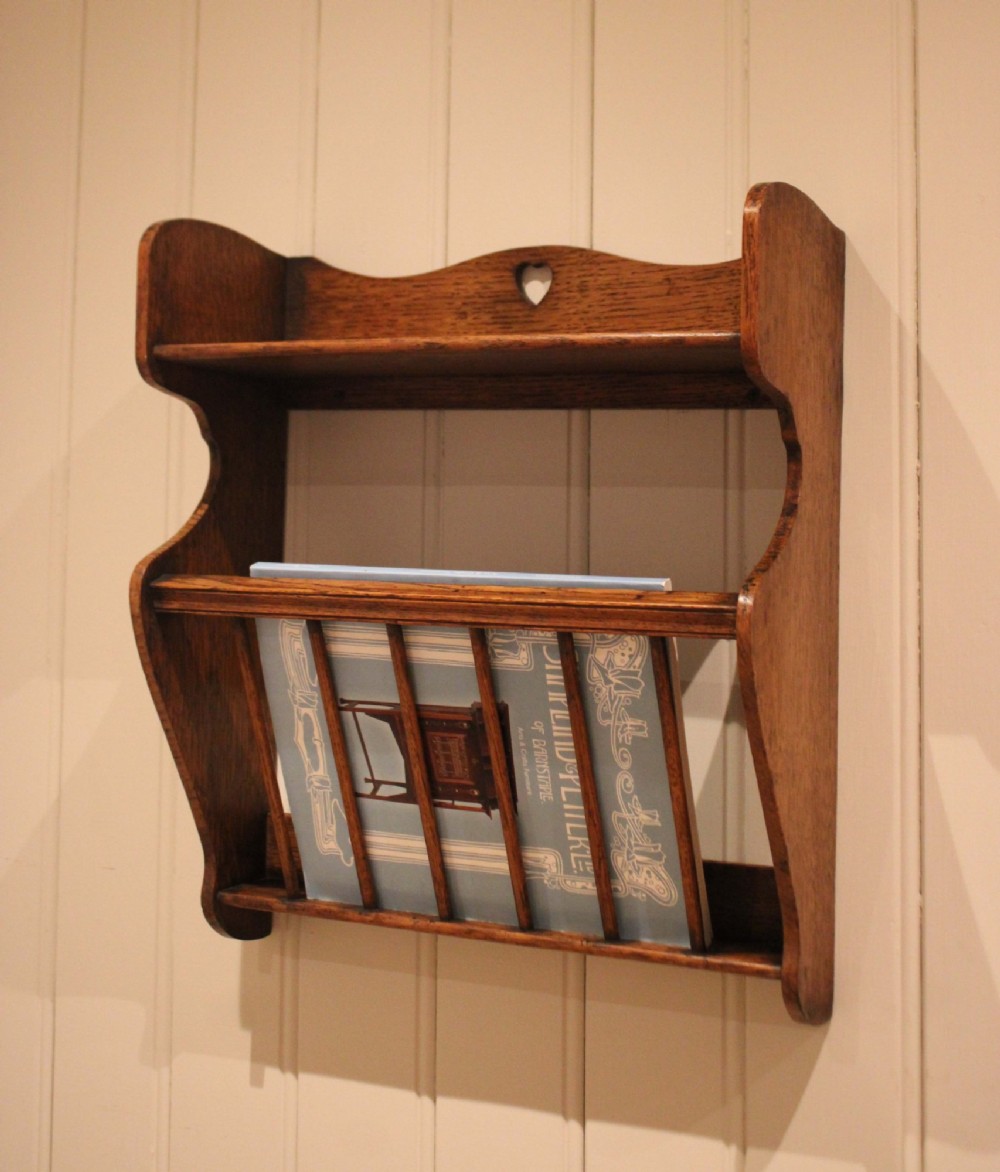 An Arts and Crafts solid oak wall shelf featuring a top shelf ledge with a pierced heart cutout and a lower magazine rack with vertical wooden spindles. View III