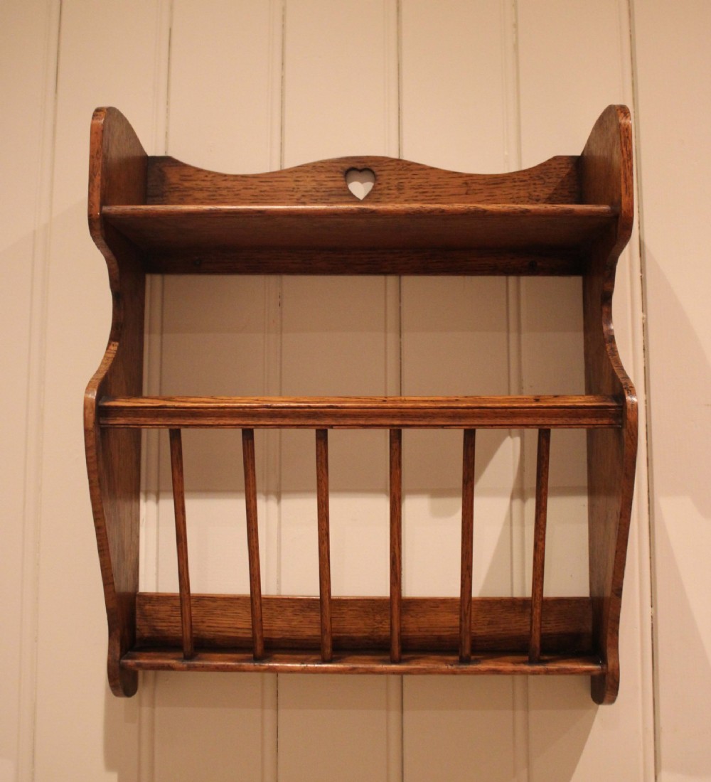 An Arts and Crafts solid oak wall shelf featuring a top shelf ledge with a pierced heart cutout and a lower magazine rack with vertical wooden spindles. View IV