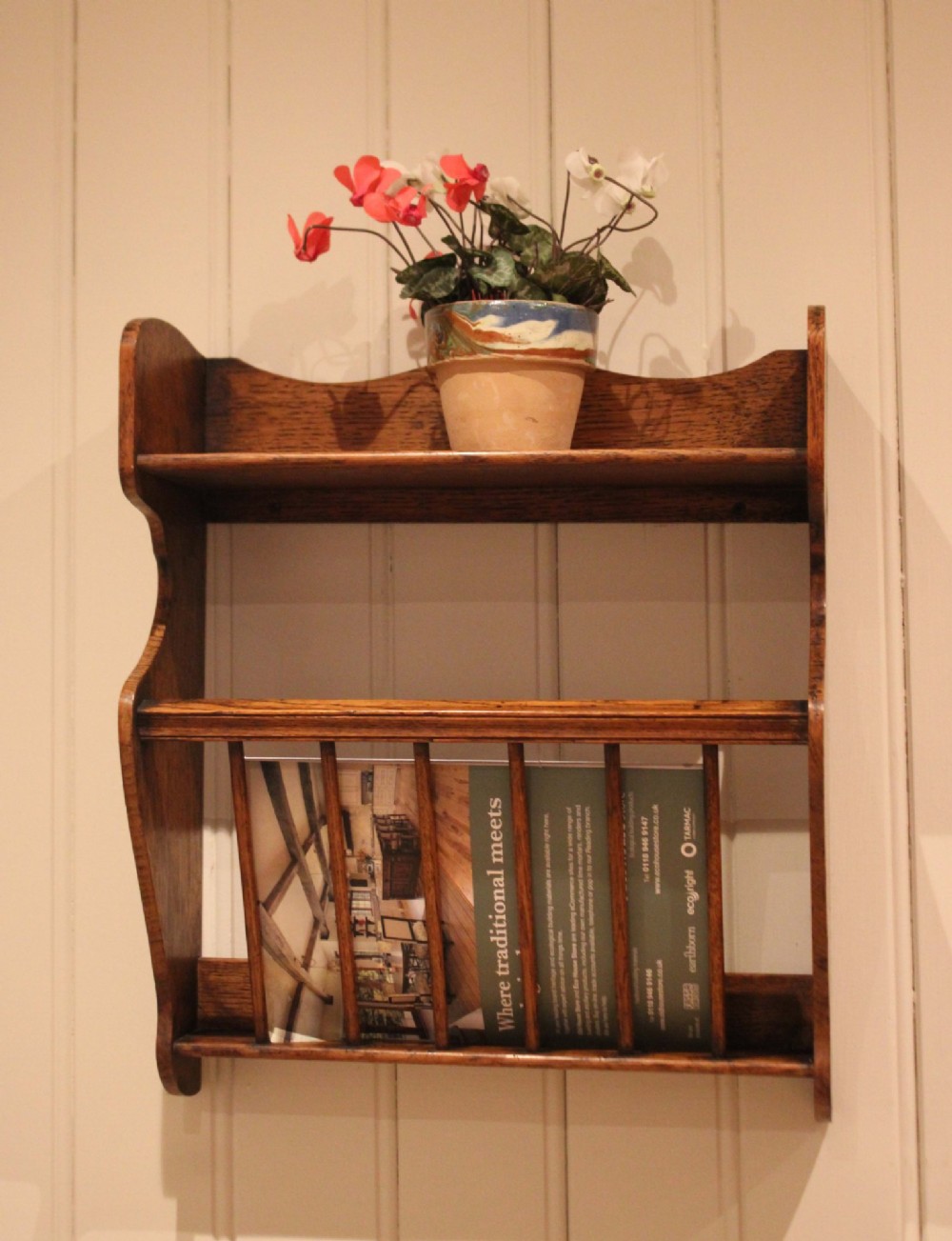 An Arts and Crafts solid oak wall shelf featuring a top shelf ledge with a pierced heart cutout and a lower magazine rack with vertical wooden spindles. View V
